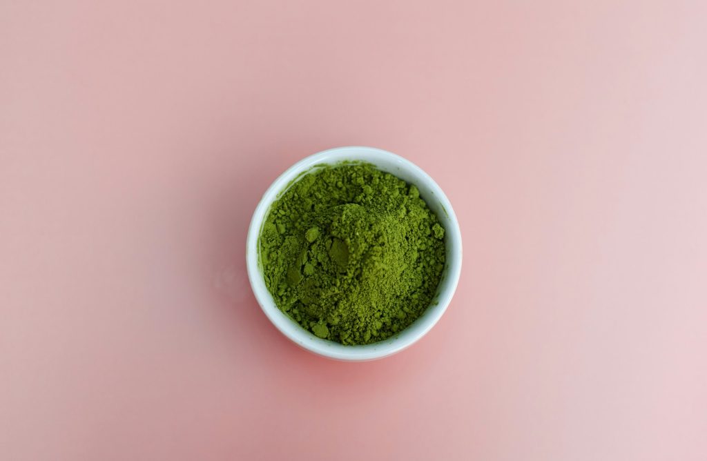 a bowl of green powder in front of a pink background