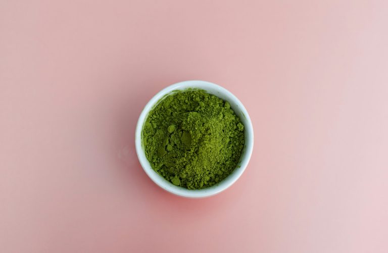 a bowl of green powder in front of a pink background